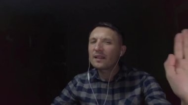 Genç bir adam karanlık odasında bir kulaklıkla müzik dinliyor.