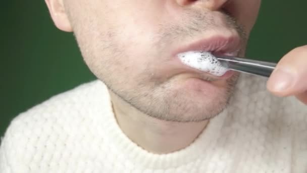 Νεαρός που βουρτσίζει τα δόντια του με μαύρη οδοντόβουρτσα, κοντά σε πράσινο φόντο. — Αρχείο Βίντεο