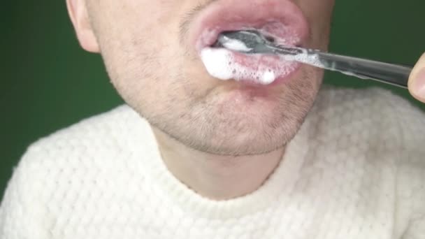 Jeune homme se brossant les dents avec une brosse à dents noire, gros plan sur fond vert — Video