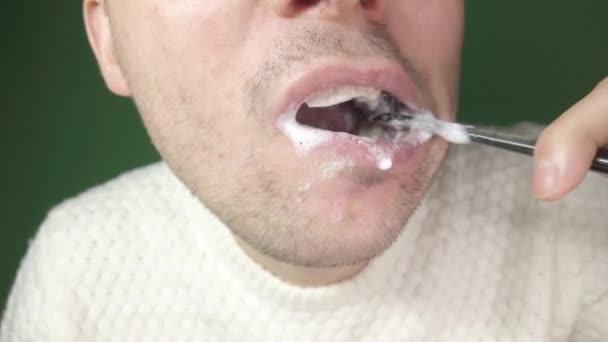 Mladý muž si čistí zuby černým kartáčkem na zuby, zblízka na zeleném pozadí — Stock video