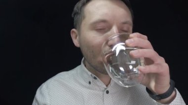 Bir adam siyah arka planda şeffaf bir bardaktan su içer.