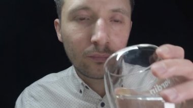Bir adam siyah arka planda şeffaf bir bardaktan su içer.