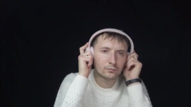 Pembe kulaklıklı bir adam siyah arka planda müzik dinliyor.