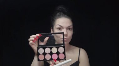 Kız kendi makyajını yapıyor, yüzüne bakıyor ve güzellik yaratıyor. Siyah arkaplanda makyajlı görüntüler.