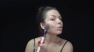 Kız kendi makyajını yapıyor, yüzüne bakıyor ve güzellik yaratıyor. Siyah arkaplanda makyajlı görüntüler.