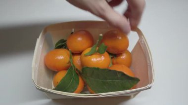 Tahta sepetteki mandalinalar, bir insan elleriyle mandalinaya dokunur.