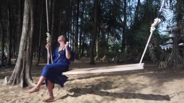 Bir kız kumlu bir sahilde büyük bir salıncakta sallanıyor.