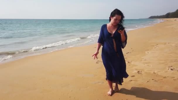 Mooie Brunette Loopt Een Lange Verlaten Strand Kijkt Haar Telefoon — Stockvideo