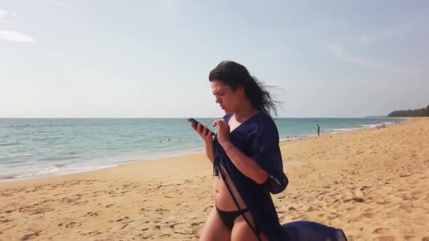 Hermosa Morena Camina Una Larga Playa Desierta Mira Teléfono — Vídeos de Stock