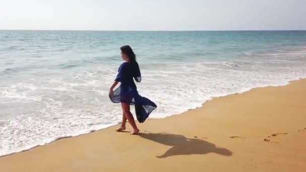美丽的黑发姑娘走在一片荒芜的海滩上 看着她的手机 — 图库视频影像