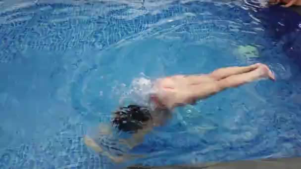 Красивая девушка в оранжевом купальнике плавает в голубом бассейне — стоковое видео