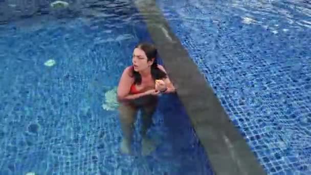 Красива дівчина в помаранчевому купальнику плаває в блакитному басейні — стокове відео