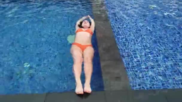 Hermosa chica en traje de baño naranja nada en la piscina azul — Vídeo de stock