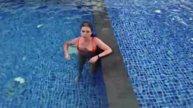 Turuncu mayo giyen güzel kız mavi havuzda yüzüyor.