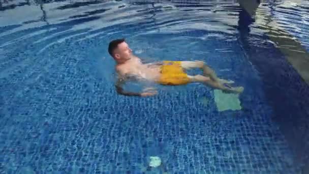 Татуированный мужчина плавает в голубом бассейне — стоковое видео