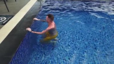 Dövmeli adam mavi havuzda yüzer.