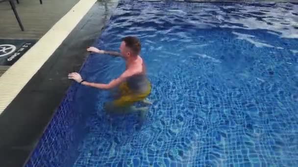 Tatuerad man simmar i blå pool — Stockvideo