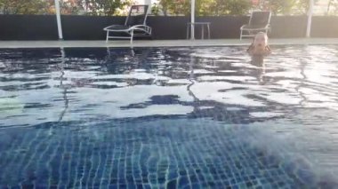 Kız otel havuzunda yüzüyor. Kız havuz kenarında dinleniyor.