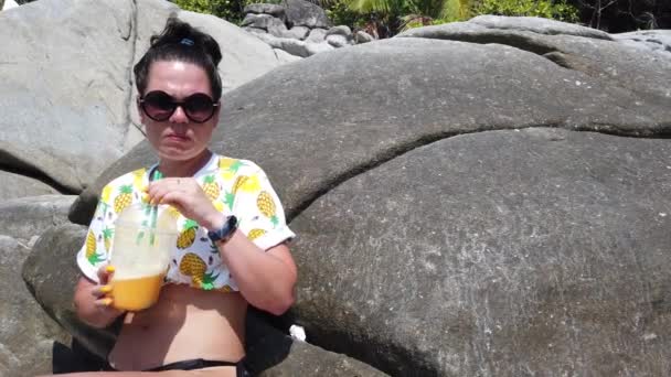 Fată Bea Fructe Proaspete Plajă Așezată Piatră Mare Fundalul Tropicelor — Videoclip de stoc