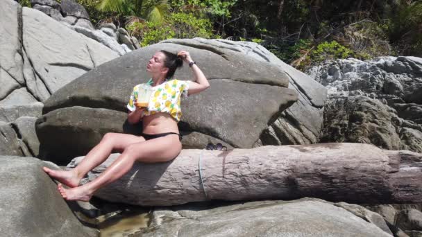 Una Chica Bebe Fruta Fresca Playa Sentada Una Gran Piedra — Vídeo de stock