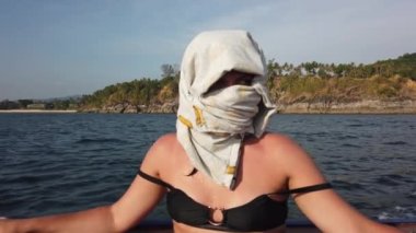 Sahilde koşuşturan bir kız yüzünü güneşten gelen kıyafetlerle kaplıyor.