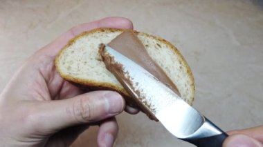 Ağır çekim adam ciabatta dilimine çikolata fındık ezmesi sürüyor.