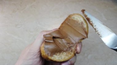 Ağır çekim adam ciabatta dilimine çikolata fındık ezmesi sürüyor.