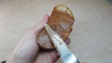Ağır çekim adam ciabatta dilimine çikolata fındık ezmesi sürüyor.