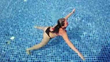 Genç esmer kız güneşli bir günde havuzda yüzer.