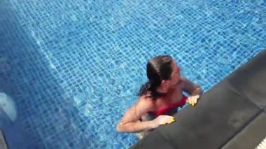 Genç esmer kız güneşli bir günde havuzda yüzer.