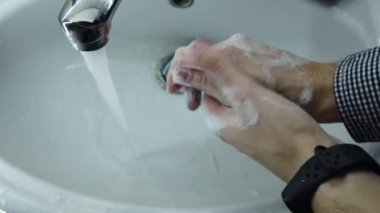 Adam ellerini banyoda sabunla iyice yıkıyor. Musluktan su akar. Enfeksiyonu önle. - Yakın çekim. Coronavirus salgını önleme sabunla sıcak suyla ellerini yıka.