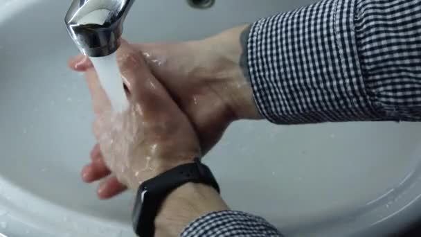 男はバスルームで石鹸で手を徹底的に洗う 水道から水が流れています 感染を防ぐ 閉鎖だ コロナウイルスのパンデミック予防温水石鹸で手を洗う — ストック動画