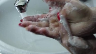 Kız ellerini banyoda sabunla iyice yıkıyor. Musluktan su akar. Enfeksiyonu önle. - Yakın çekim. Coronavirus salgını önleme sabunla sıcak suyla ellerini yıka.