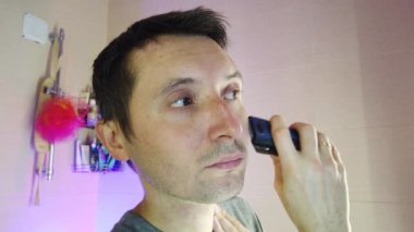 Banyodaki adam elektro jileti traş ediyor.