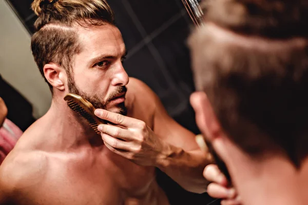 Hipster man combing beard in front of a mirror — Stock Photo, Image