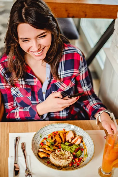 Girl laughing at the restaurant and holding mobile phone — Stock Photo, Image