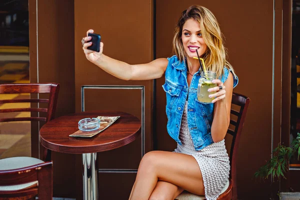 Девушка в кафе делает селфи и пьет лимонад — стоковое фото