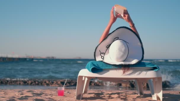 Chica acostada en la playa y leyendo un libro — Vídeo de stock