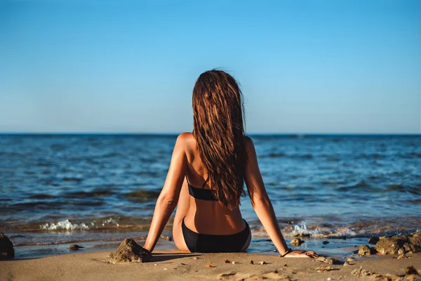 Mujer joven sentada en la playa y mirando el mar —  Fotos de Stock