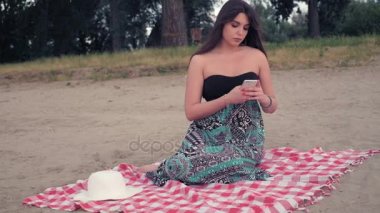 Sahilde oturan ve telefonla mesajlaşma endişeli kız