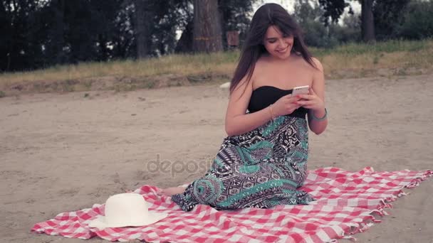 Flickan sitter på stranden, med hjälp av mobiltelefon och skrattar — Stockvideo