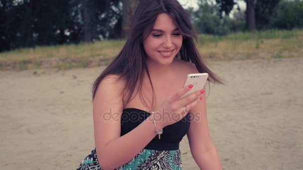 Flicka leende medan du använder telefonen på stranden — Stockvideo
