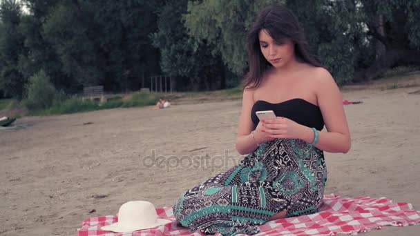 Sad girl sitting on the beach and looking at mobile phone — Stock Video