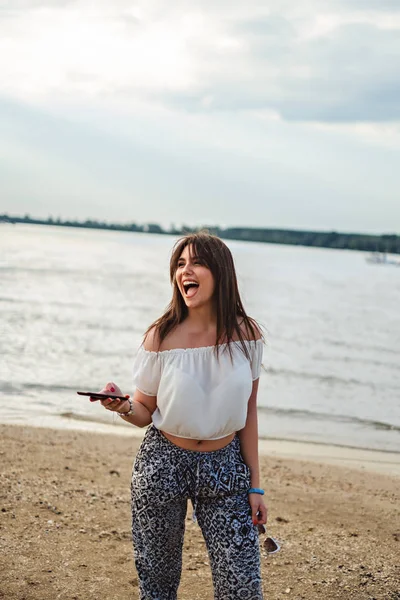 Ragazza ridendo e tenendo il telefono sulla spiaggia — Foto Stock