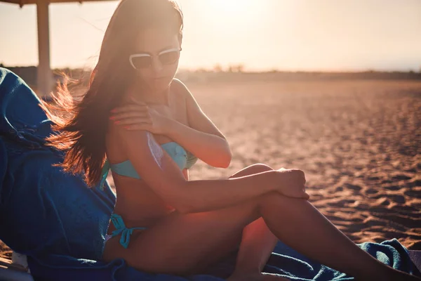 Chica aplicando crema solar mientras está sentado en la playa —  Fotos de Stock