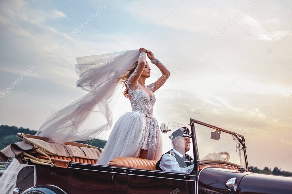 Bride standing in classic convertible while being driven