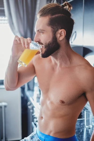 Мужчина без рубашки пьет апельсиновый сок на кухне — стоковое фото