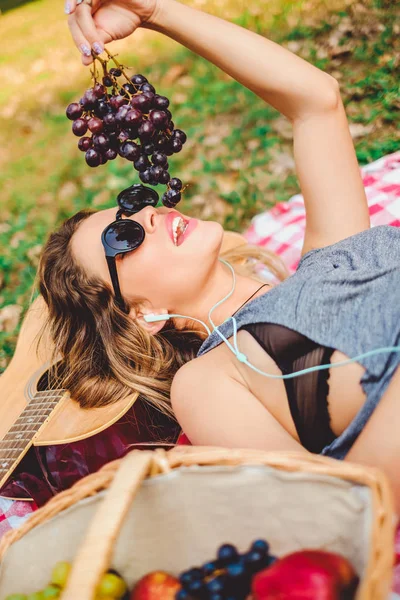 Ragazza sdraiata su una chitarra e mangiare uva su picnic — Foto Stock