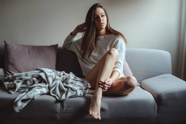 Sexy chica en suéter sentado en un sofá y pensando — Foto de Stock