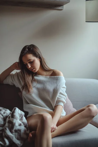 穿着毛衣的性感女孩独自坐在沙发上 — 图库照片